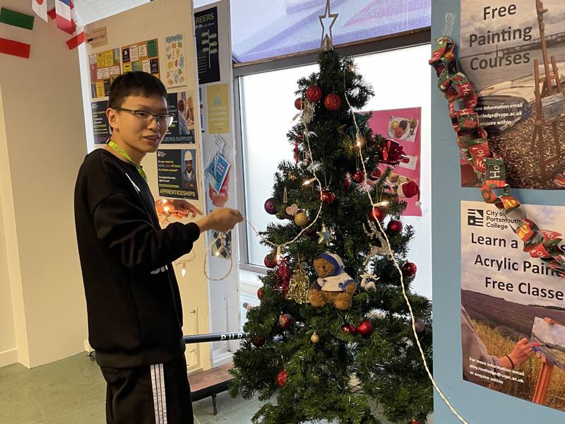 Male student putting the lights on a Christmas tree.