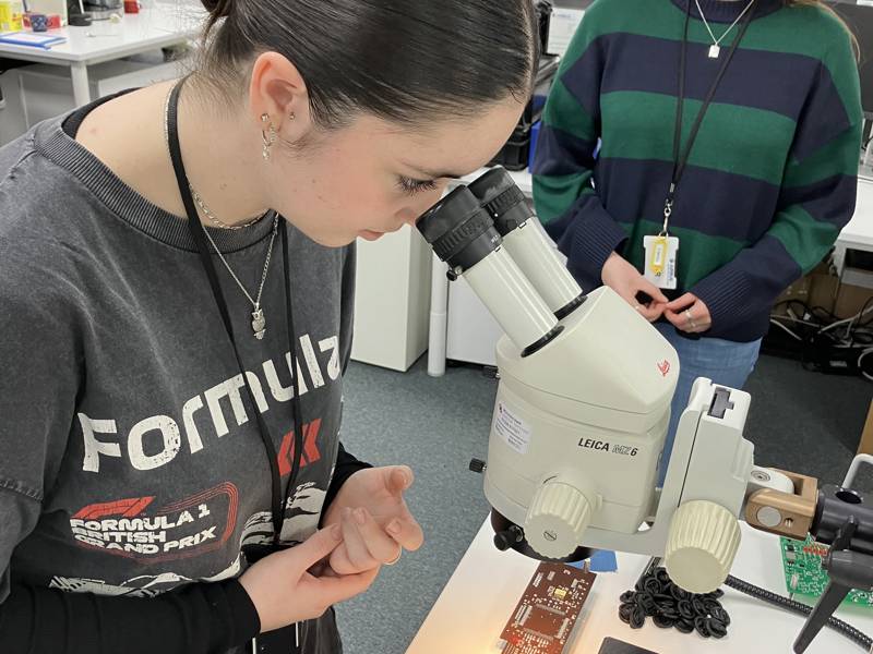 Student is seen looking through a microscope while another looks on.