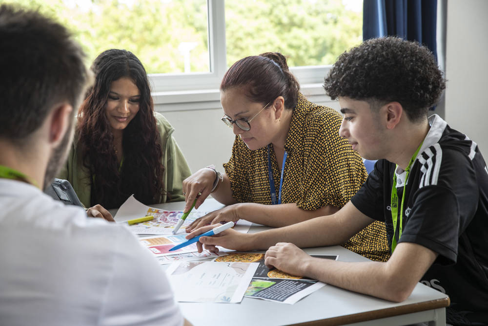 A group of students studying at a classroom table with a lecturer. 