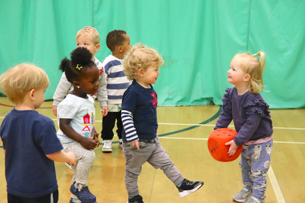 Young nursery goers playing with giant dice in the sports hall.