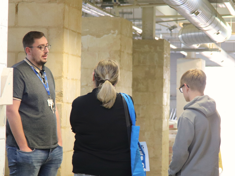 Prospective student and parent talking to staff member in plastering workshop.