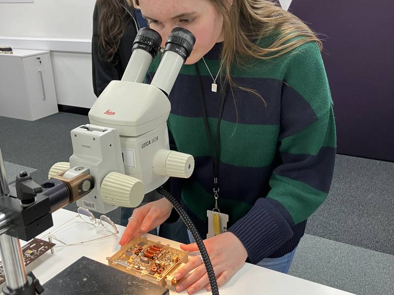 Another student examines a component under a microscope.