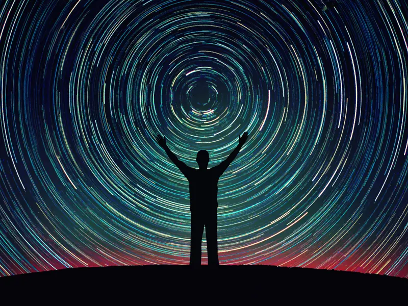 Person silhouette on a night sky background with bright stars trails