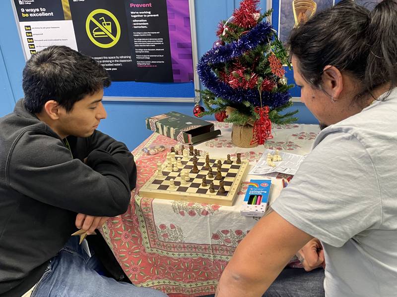 ESOL students playing chess in front of a small, decorated Christmas tree.