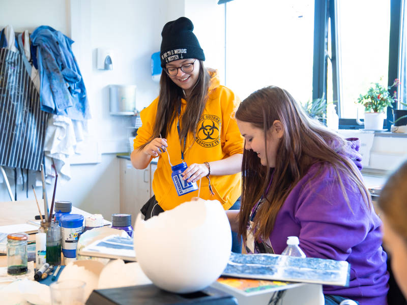 Art students smiling while working with mixed media in Art Studio.